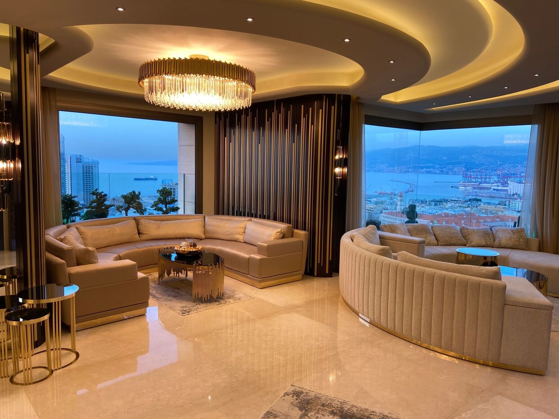 A finished Tanfeez living room with curved sofas, a crystal chandelier and sea views